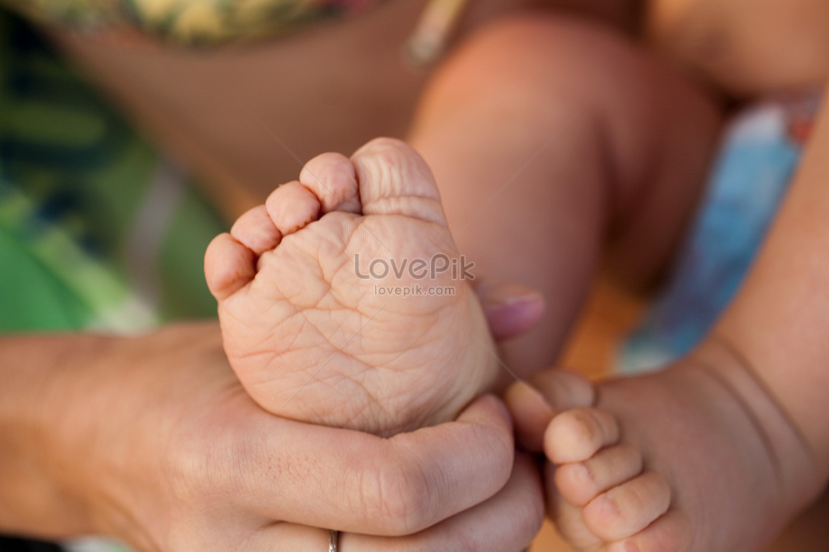 Closeup of mother hands holding cute tiny baby feet, showing baby foot.  Pink Background. Horizontal. Stock Photo