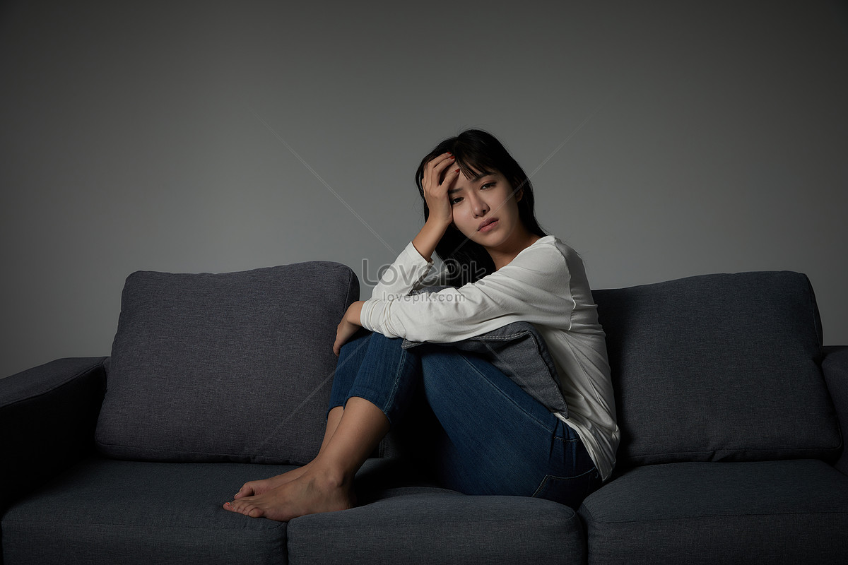 悲伤的女人抱着她的膝盖，独自坐在黑暗的房间里哭泣。高清摄影大图-千库网