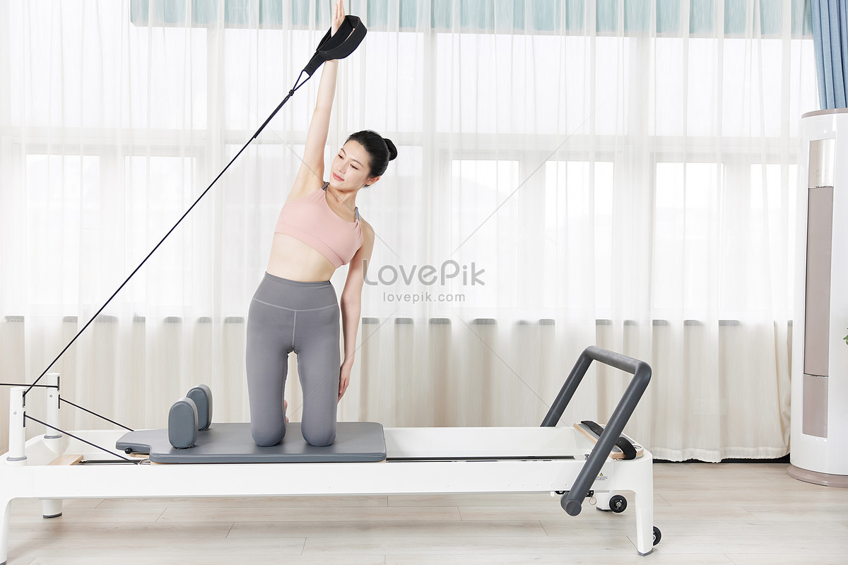 Premium Photo  Young woman doing pilates exercises with a reformer bed.  beautiful slim fitness trainer