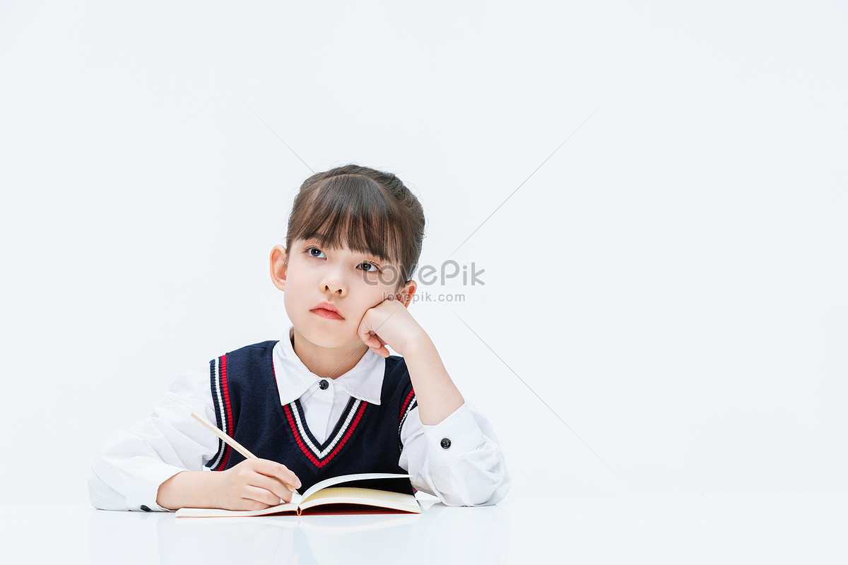 Little girl studying at the desk doing homework thinking Photo