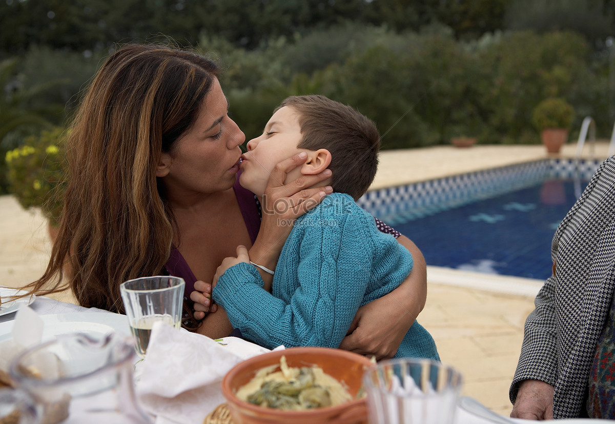Мать целует сына за столом.