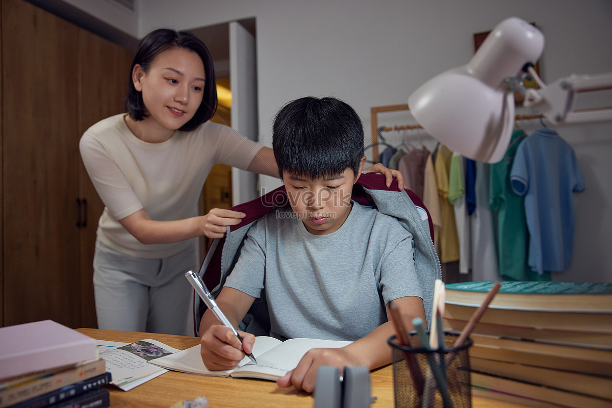 Mom adds clothes to boy who is doing homework Photo