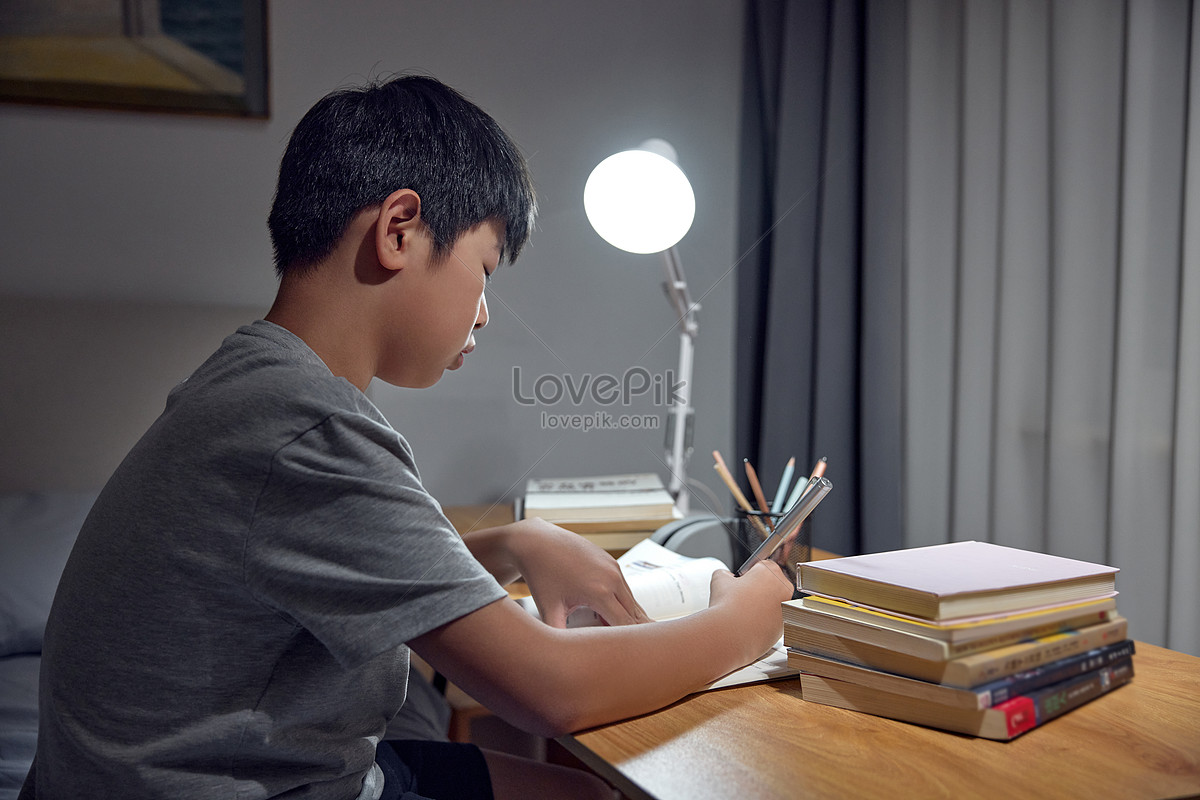 Boy doing homework under desk lamp Photo