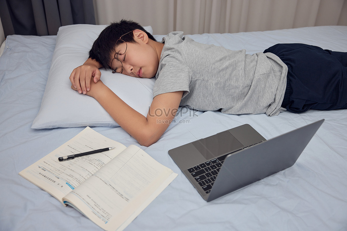Boy stayed up late doing homework and fell asleep on the bed Photo