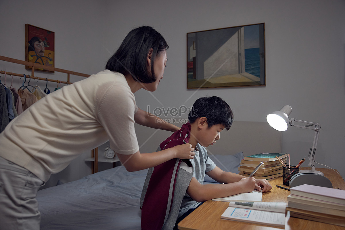 Mother puts a coat on the boy who is doing homework Photo